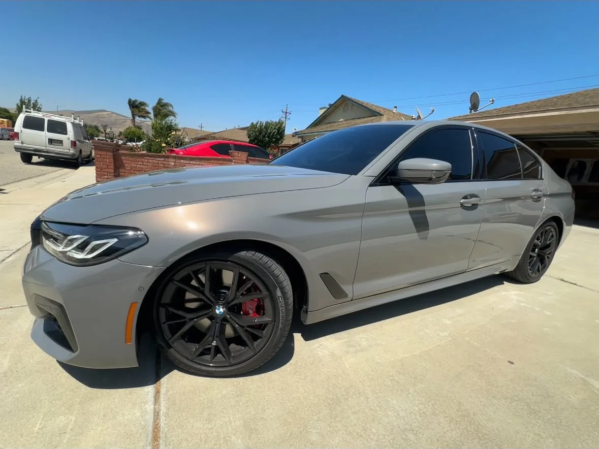 A grey BMW sedan on black wheels with red calipers, film on the doors and quarter glass