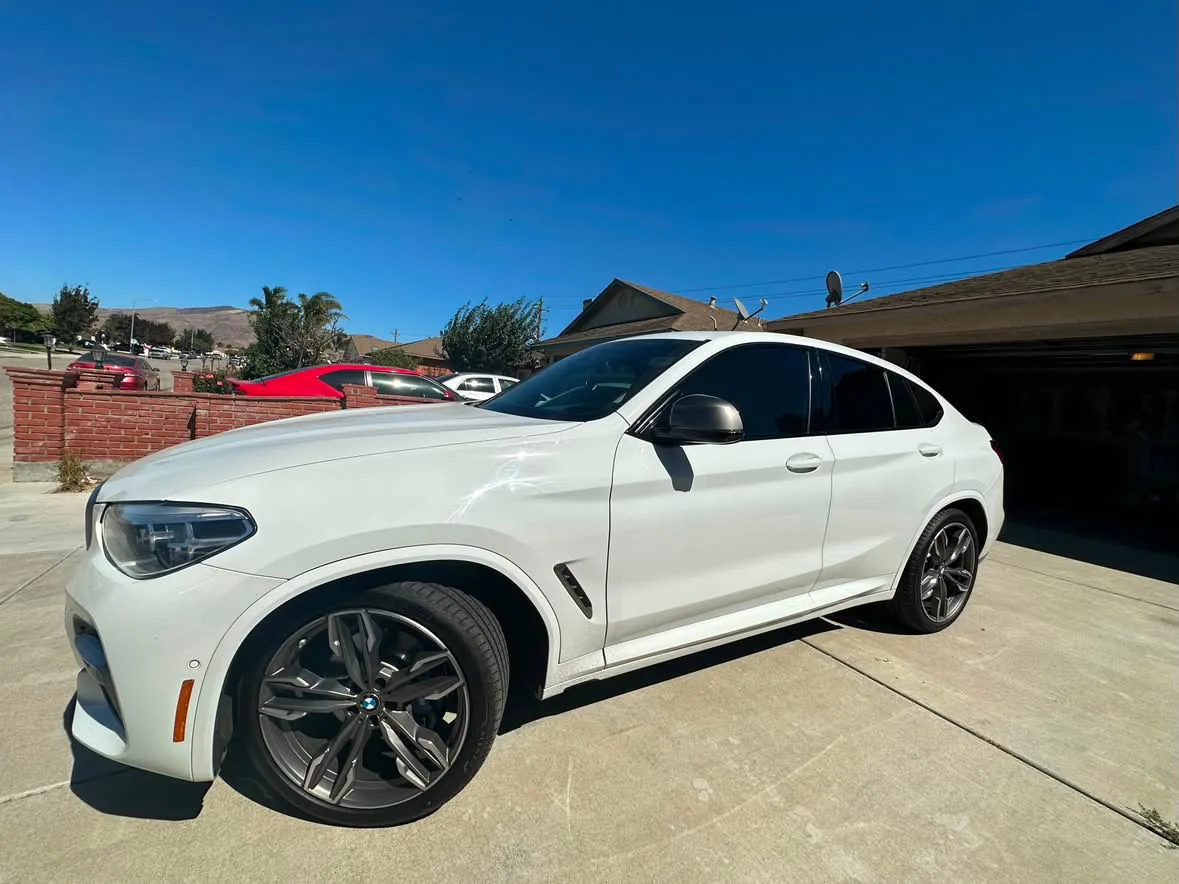 A white BMW coupe crossover outside a garage, film on the doors and quarter glass