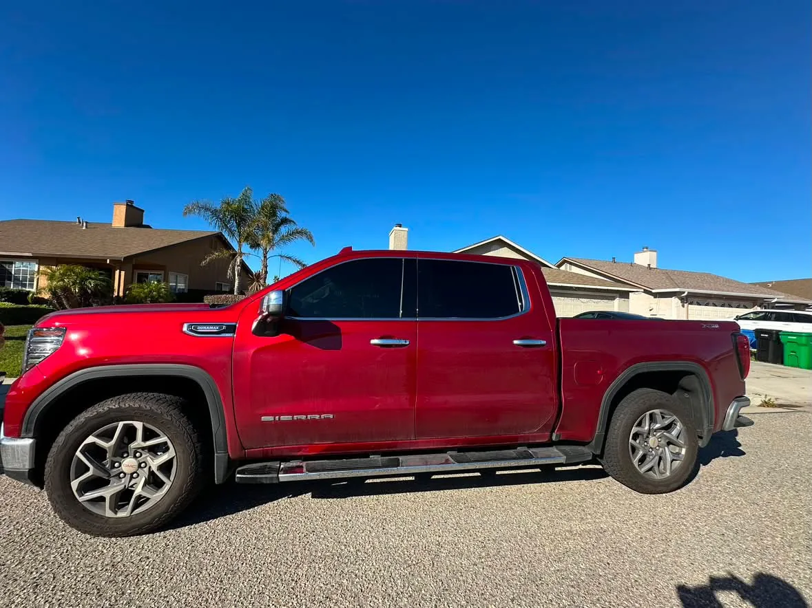 A red GMC Sierra Duramax pickup in profile with film on the door and cab glass