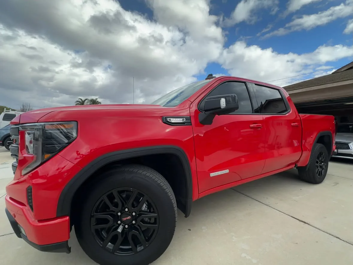 A red GMC Duramax pickup with black wheels and trim, film on both door windows