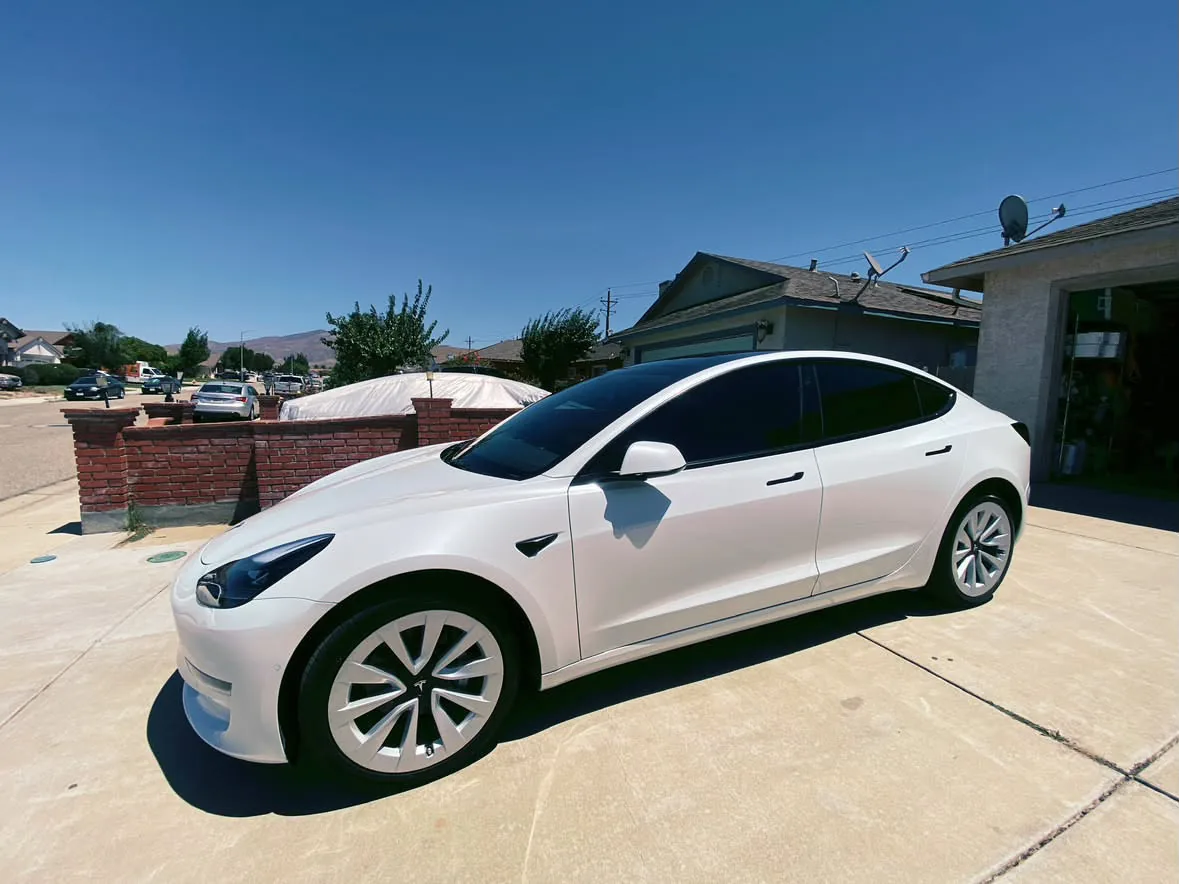 A white Tesla Model 3 in a driveway with film on the doors and rear quarter glass