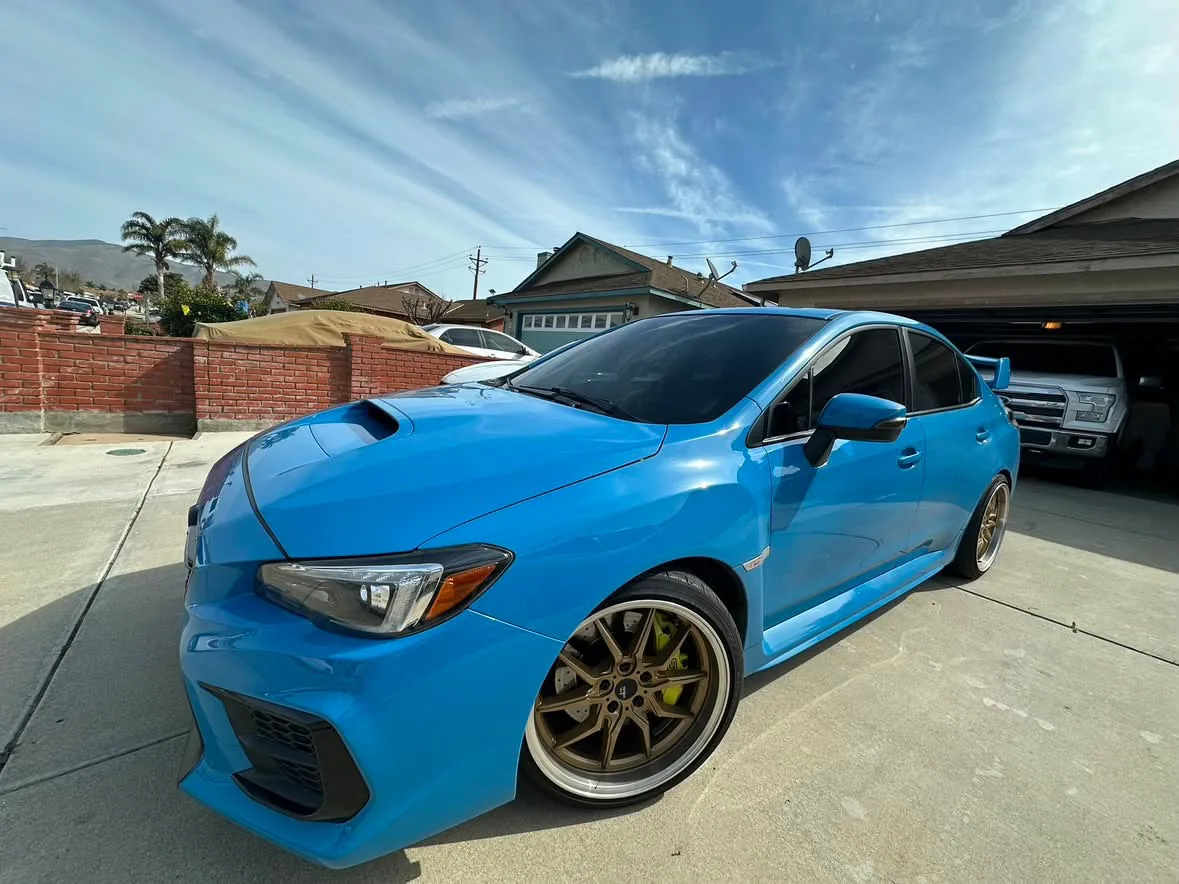 A light blue sport sedan with a bonnet scoop, pedestal rear wing and bronze wheels, film on the windscreen and all four doors